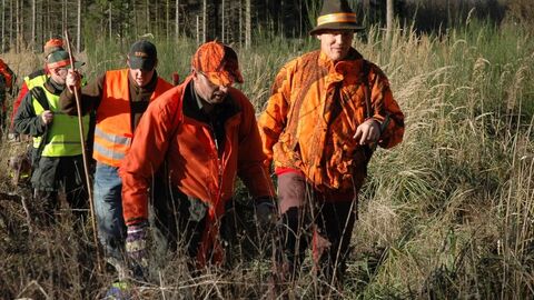 Jäger und Treiber auf Bewegungsjagd Man sieht fünf Männer im Wald.